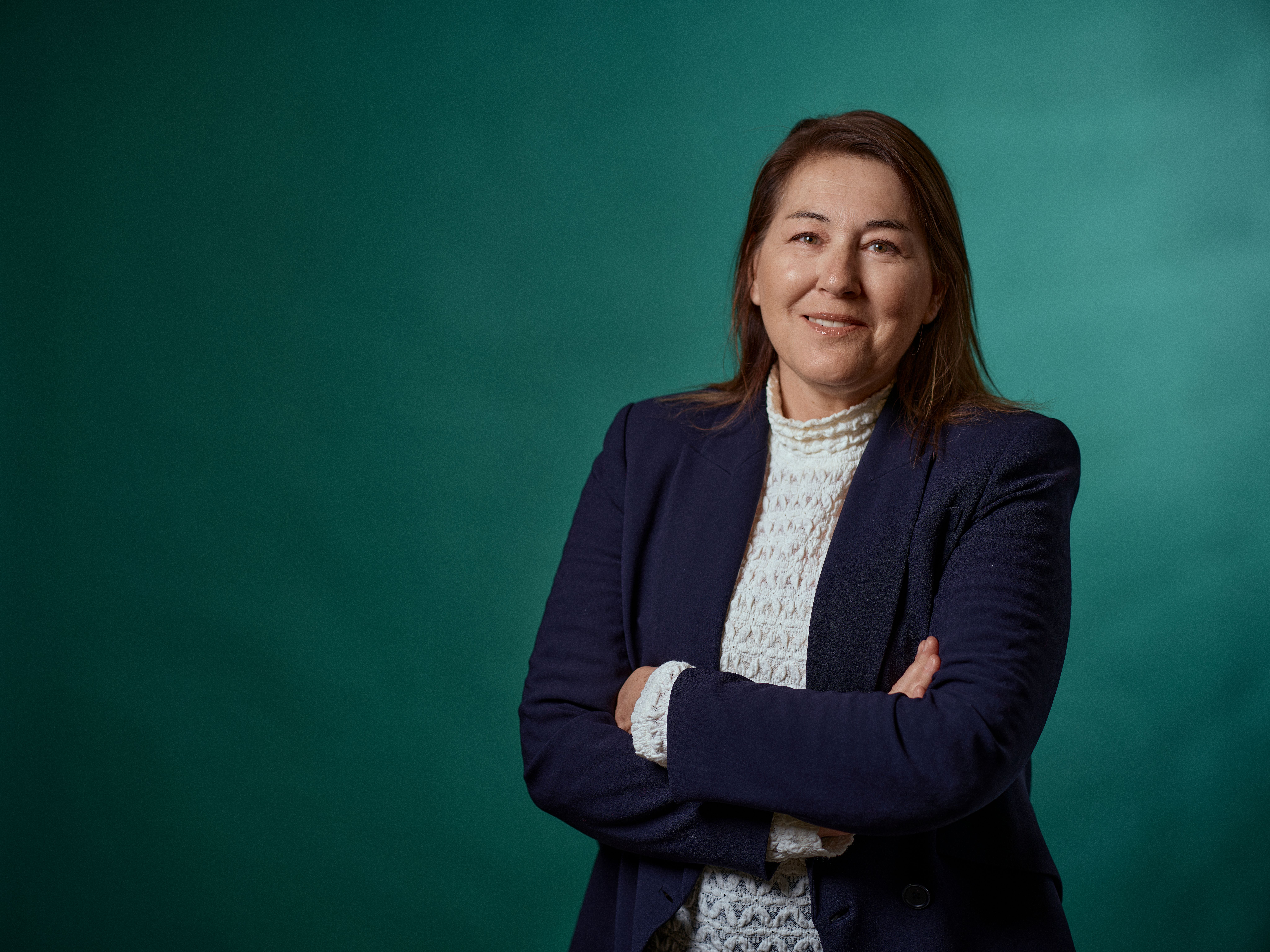 a woman in a blue jacket and white sweater is standing with her arms crossed .