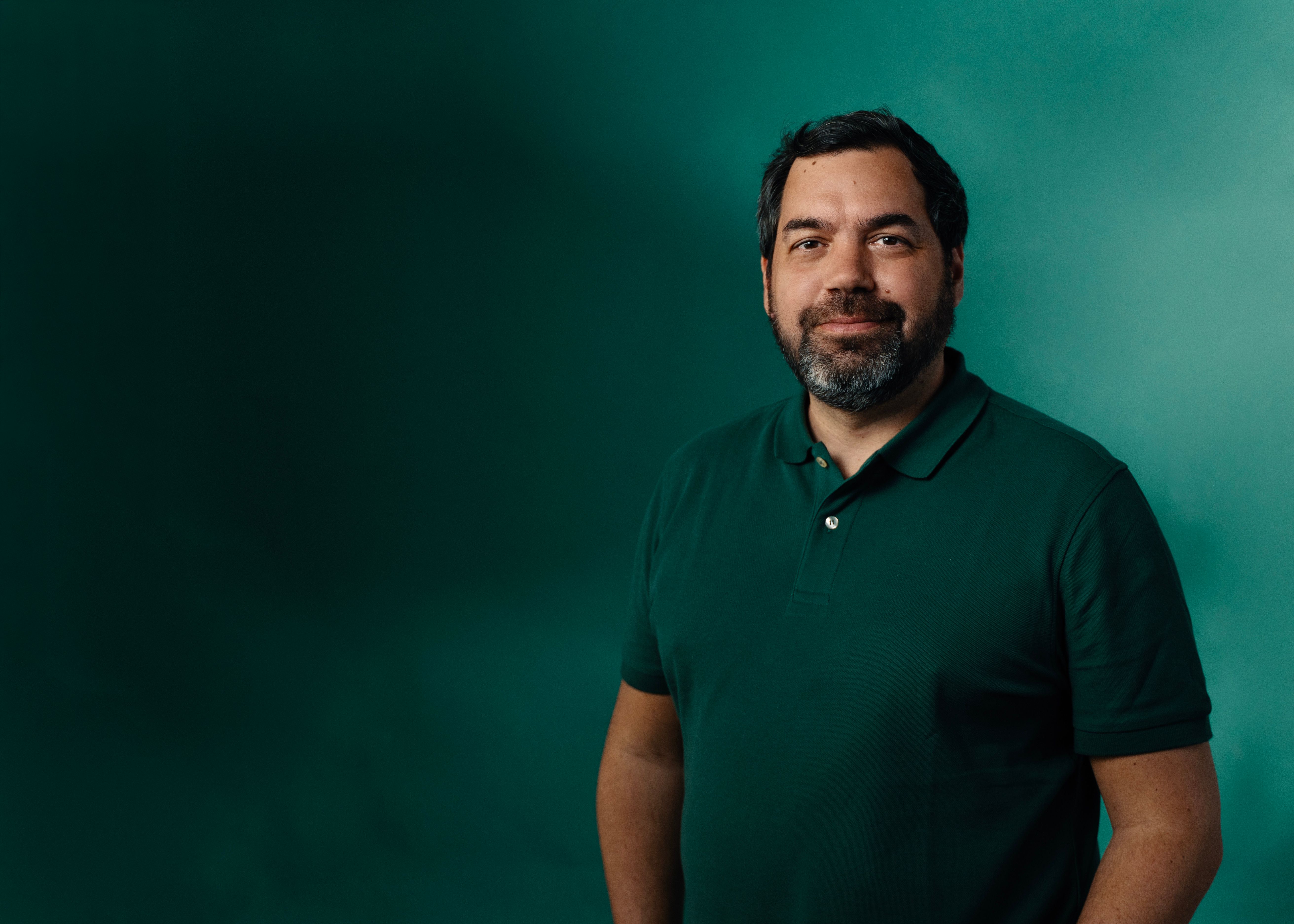 a man with a beard wearing a green polo shirt is standing in front of a green wall .