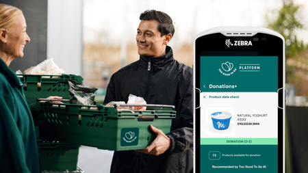 A man hands food in "Too Good To Go" crates to a woman, with a Zebra device showing the "Too Good To Go Platform" donations app.