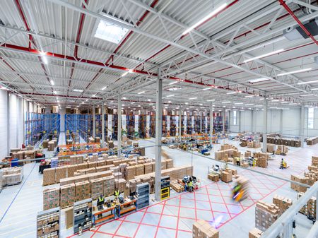 Modern, active warehouse with stacks of boxes, tall racks, and blurred workers.