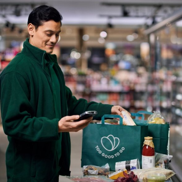 a man is looking at his phone while holding a bag that says too good to go