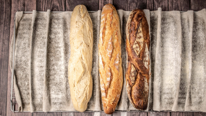 Three baguettes, light to dark, on a floured proofing cloth.