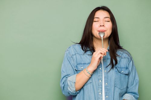 a woman is holding a spoon in her mouth with her eyes closed .