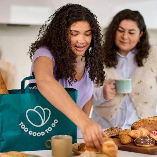 a woman is putting a croissant on a table while another woman looks on .