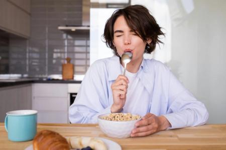 A woman is sitting at a table eating cereal with a spoon.