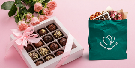 Assorted chocolates and pink roses next to a Too Good To Go bag filled with treats and flowers.