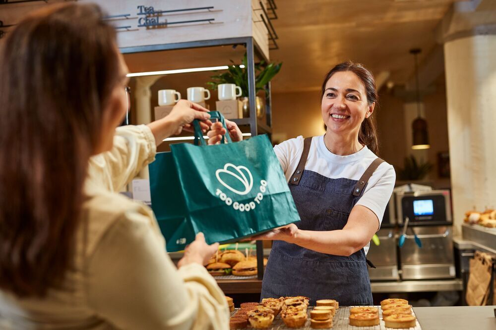 une femme donne un sac de nourriture à une autre femme dans une boulangerie.