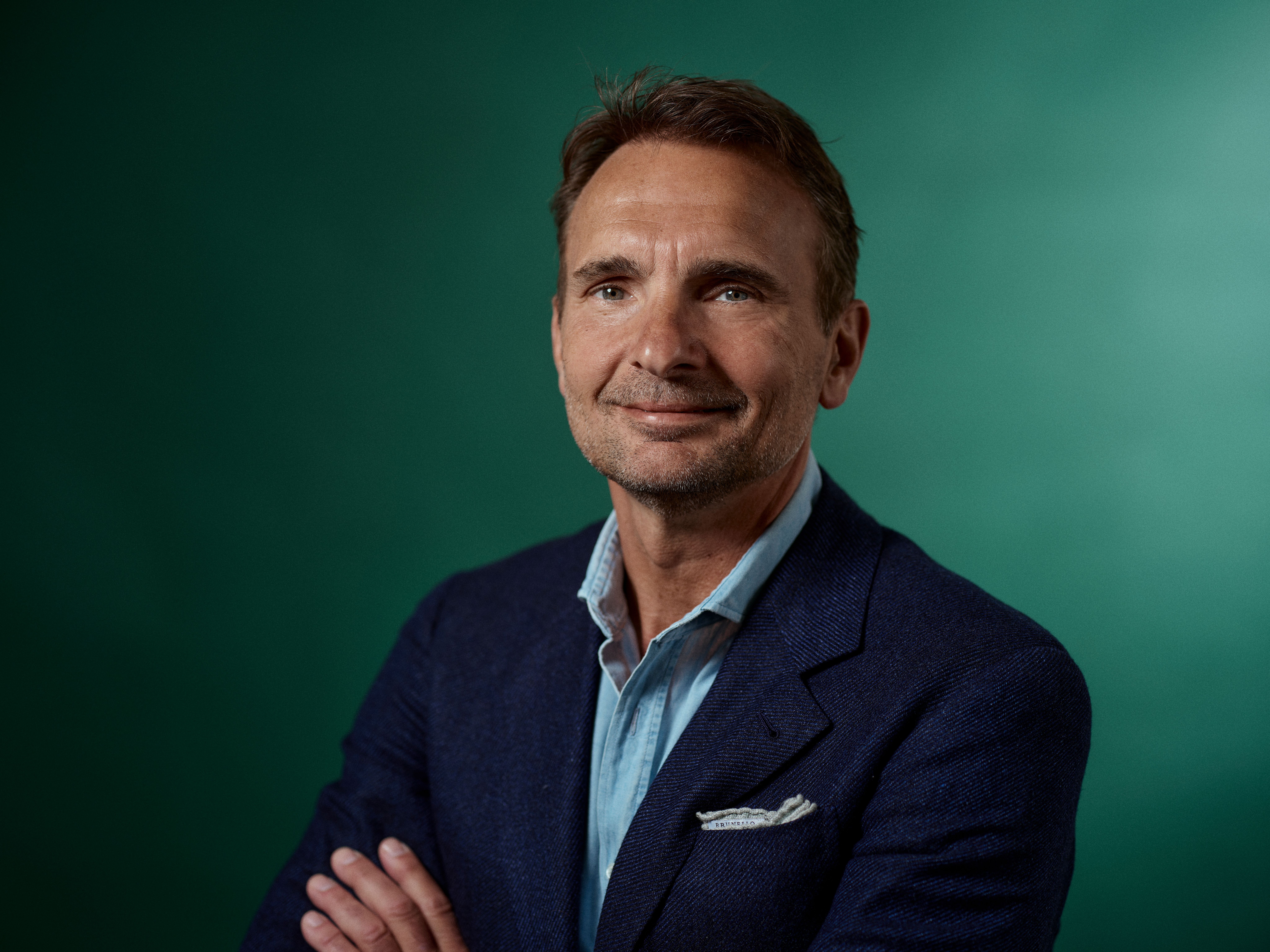a man in a suit and blue shirt is standing with his arms crossed and smiling .