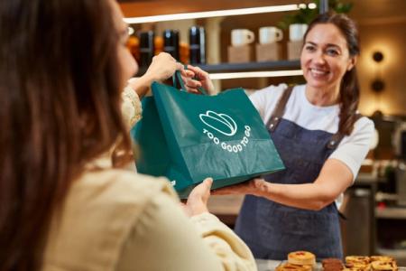 a woman is giving a bag to another woman in a bakery .