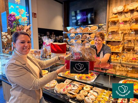 a woman is holding a bag of bread in a bakery .