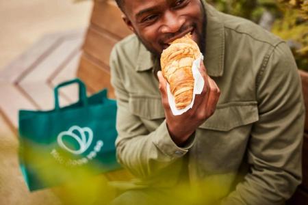 a man is sitting on a bench eating a croissant .