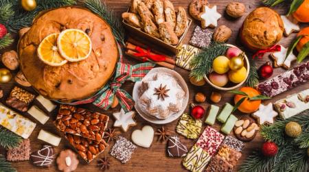 A festive spread of panettone, pandoro, cookies, and various Christmas sweets on a wooden table with pine branches and ornaments.