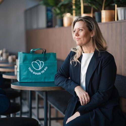 a woman sits at a table with a bag that says too good to go