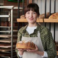 une femme tient une miche de pain dans la cuisine d'une boulangerie
