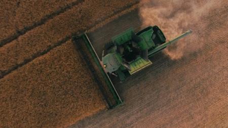 Aerial view of a green combine harvester kicking up dust in a golden field.