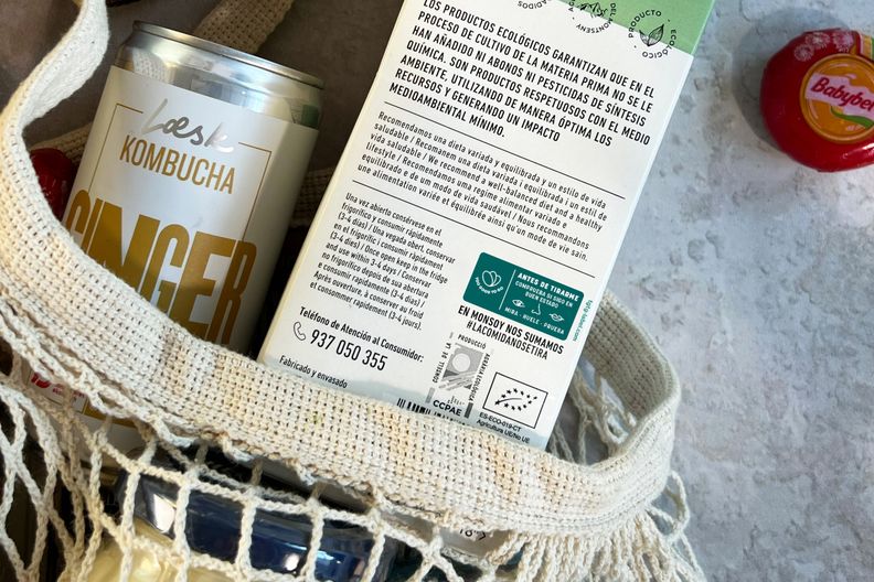 a can of kombucha is sitting in a net bag next to a bottle of kombucha .