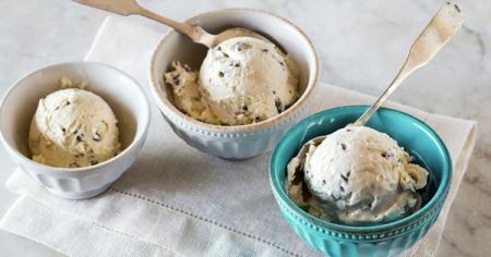 Three bowls of ice cream with spoons in them on a table.