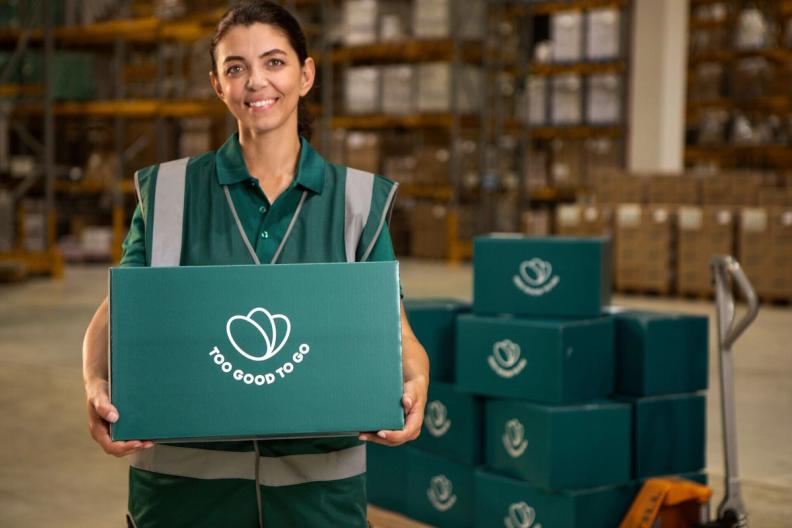 Happy Woman holding a Too Good To Go branded box and her phone