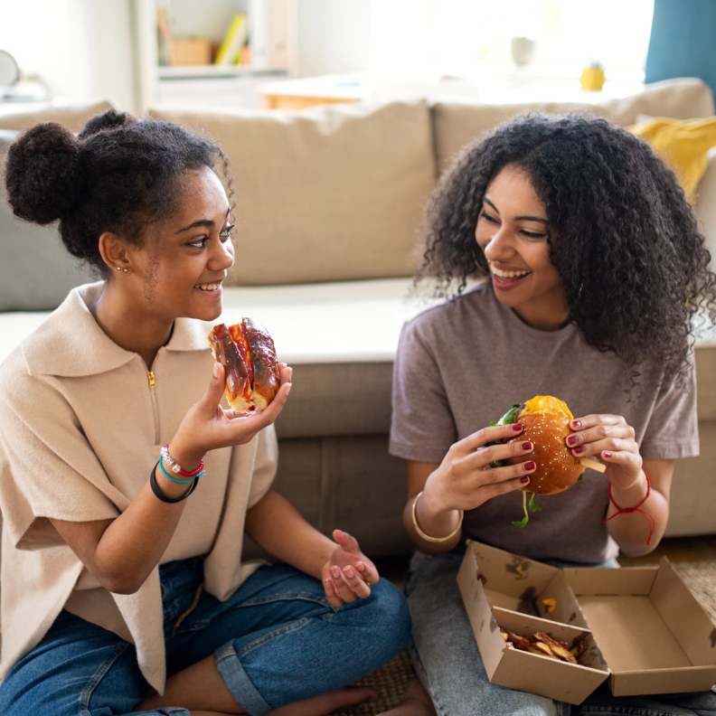 Two young women smiling and eating burgers