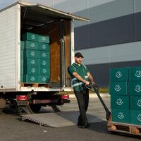 a person holding a shopping cart containing a lemon, a water bottle and other grocery items, picking up greens from the supermarket shelves