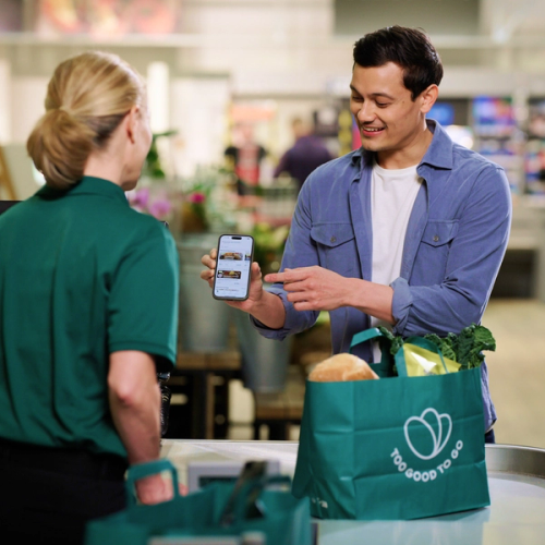 a man holding a cell phone next to a too good to go bag