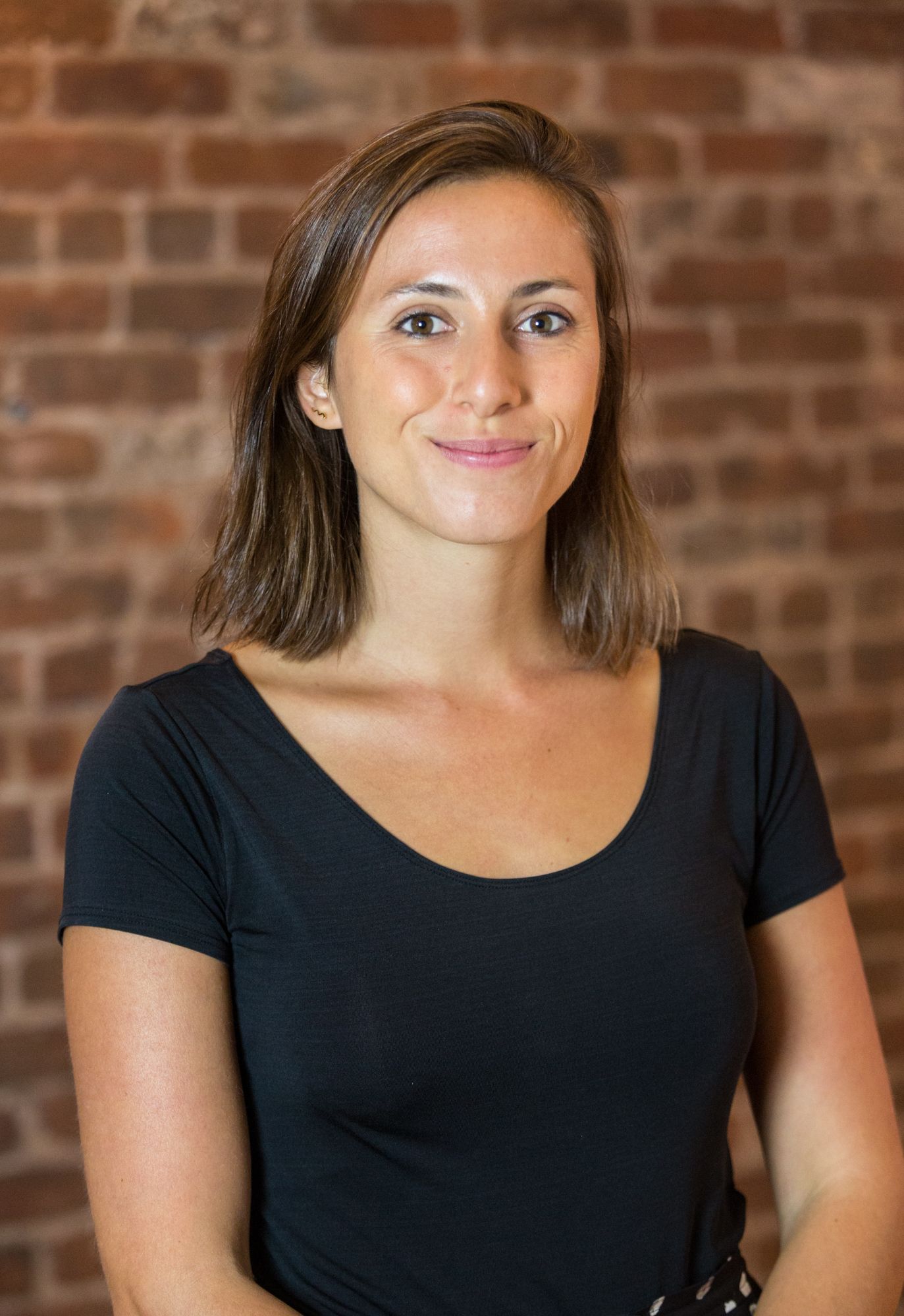 a woman in a black shirt stands in front of a brick wall