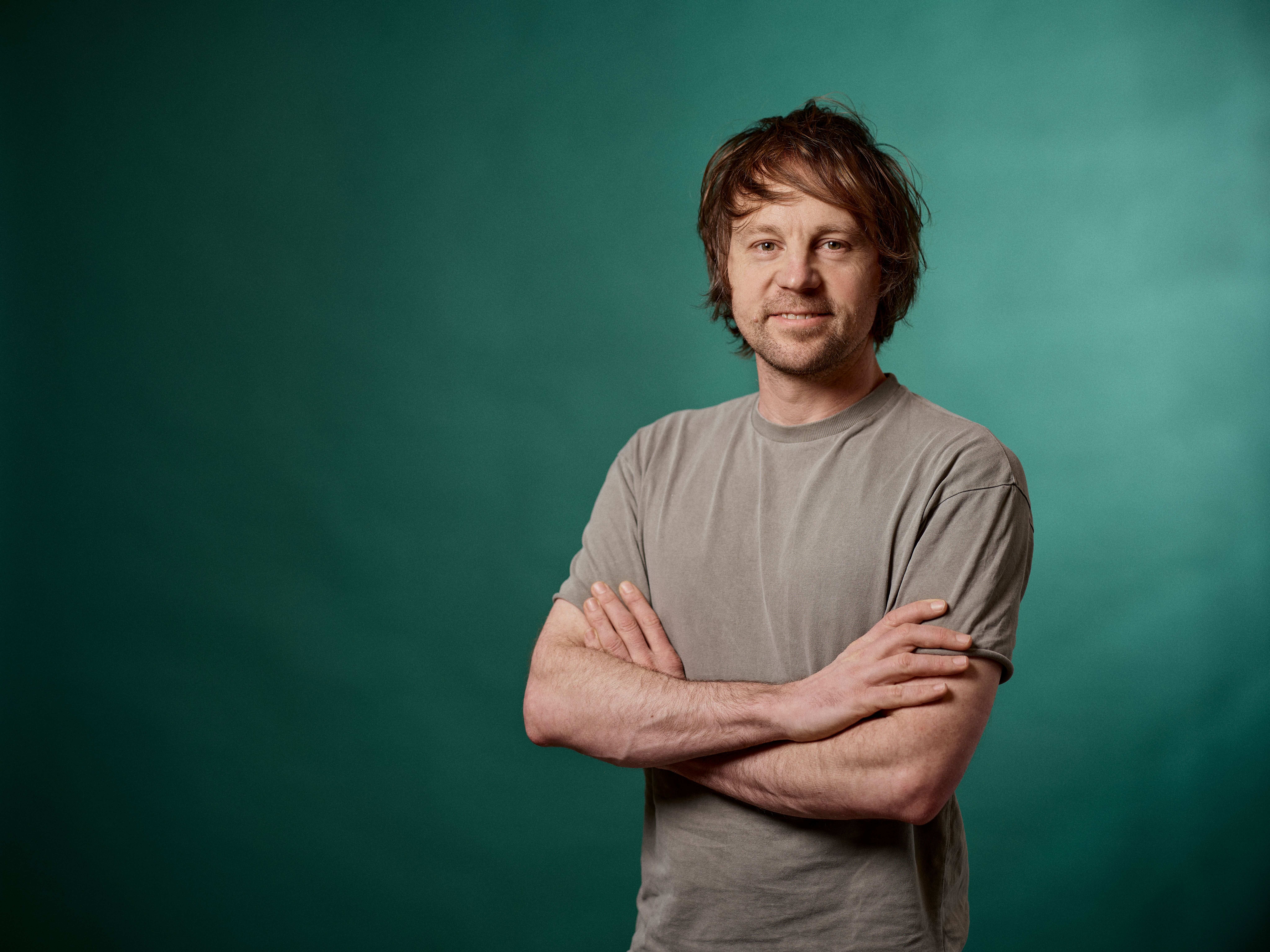 a man is standing with his arms crossed in front of a green background .