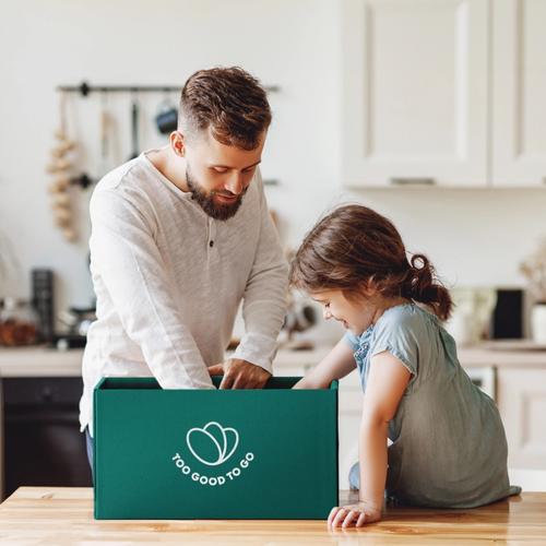 a man and a little girl are sitting at a table looking at a box .