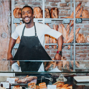 a man in an apron stands in front of a display of bread