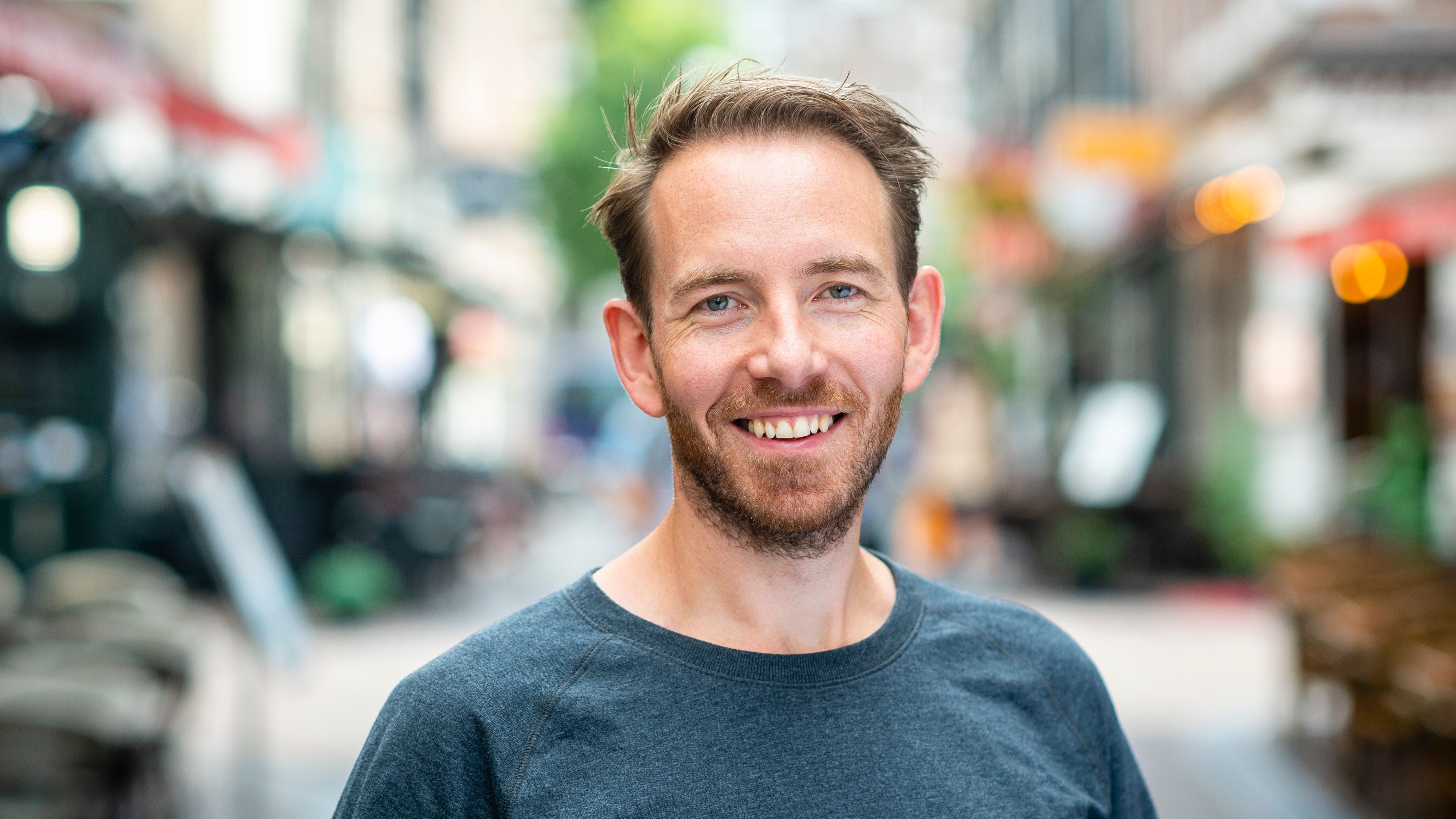 a man with a beard is smiling for the camera while standing on a city street .