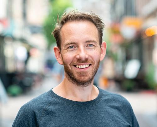 a man with a beard is smiling for the camera while standing on a city street .