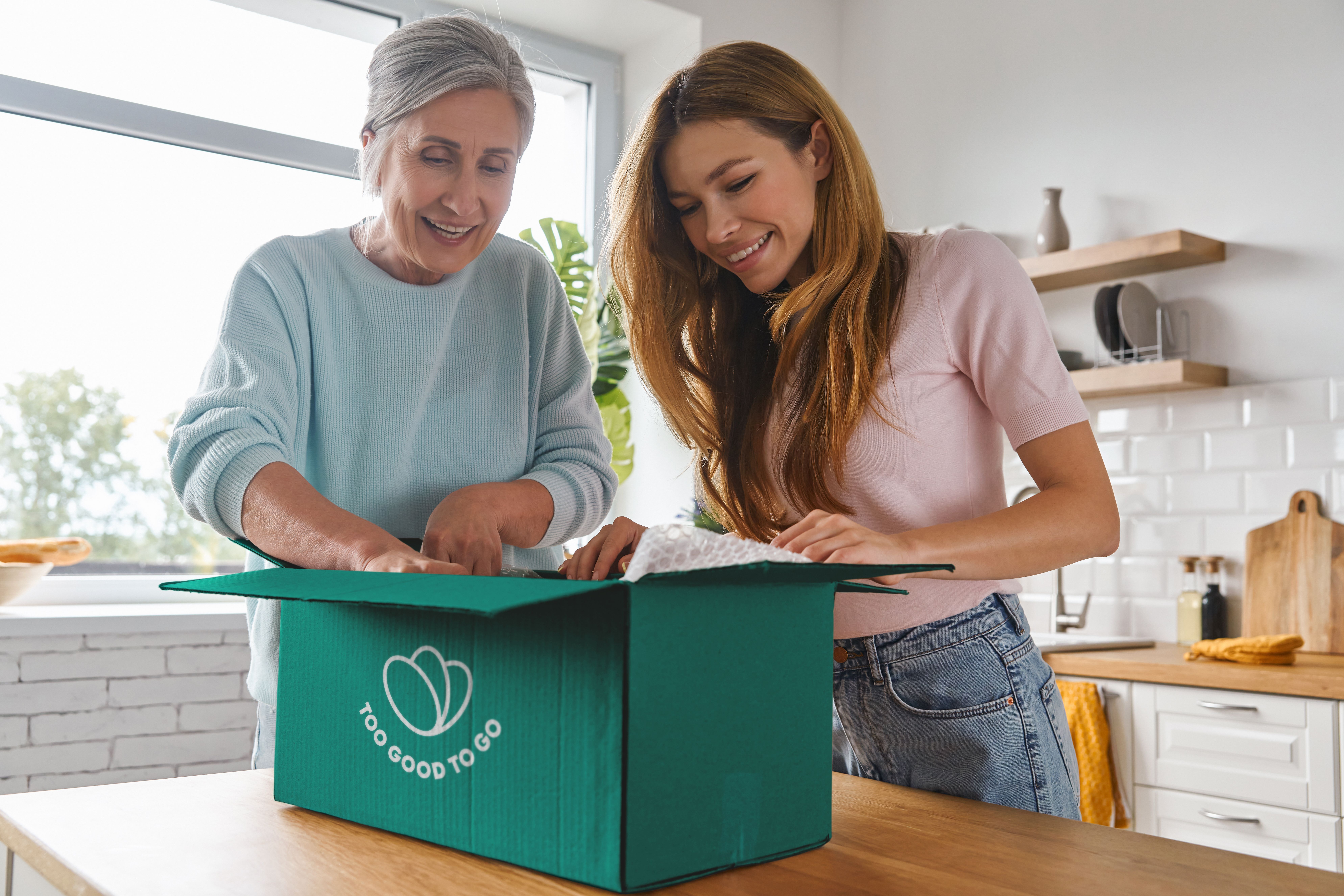 an elderly woman and a young woman are opening a box in a kitchen .