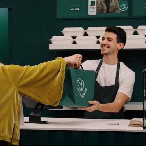 a man in an apron is giving a woman a bag of food .