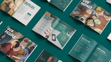 Multiple open brochures from Too Good To Go, discussing food waste and sustainability, are arranged on a teal background.