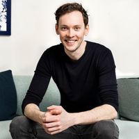 a man is sitting on a couch with his hands folded and smiling .