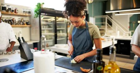 A woman in an apron chopping an onion in a professional kitchen.