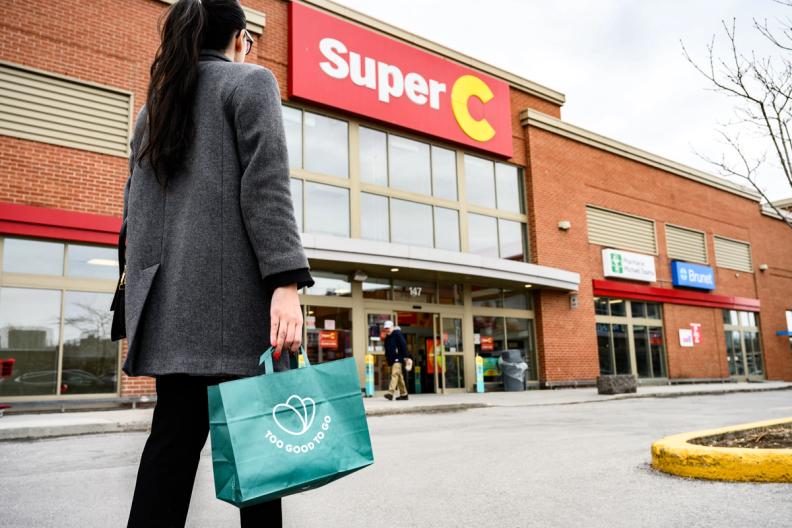 a woman is holding a green bag in front of a super c store .
