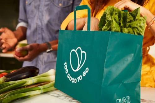 a woman is holding a bag of vegetables while a man prepares food in the background .