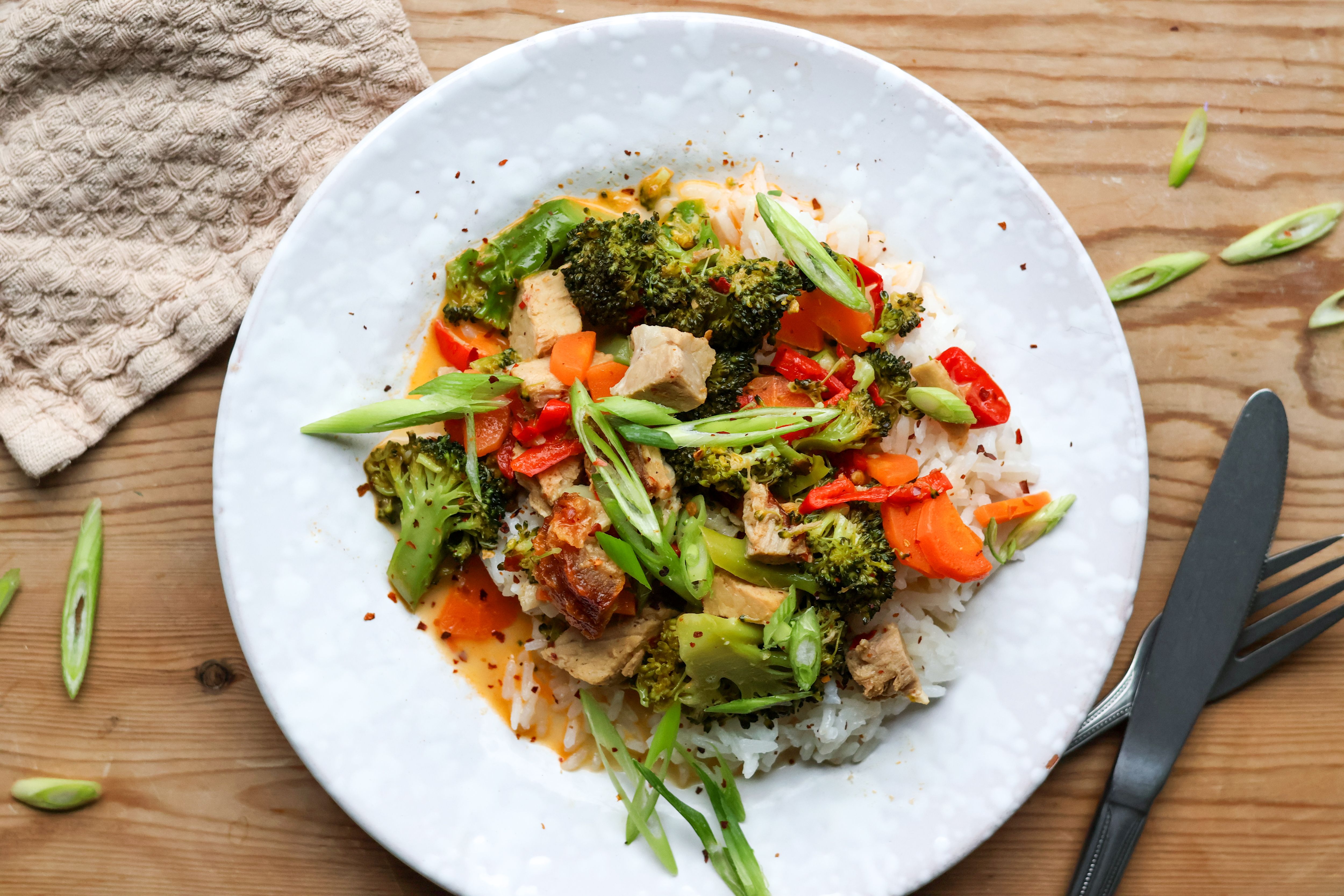 a white plate containing vegetables including broccoli and rice with a black fork and knife next to it