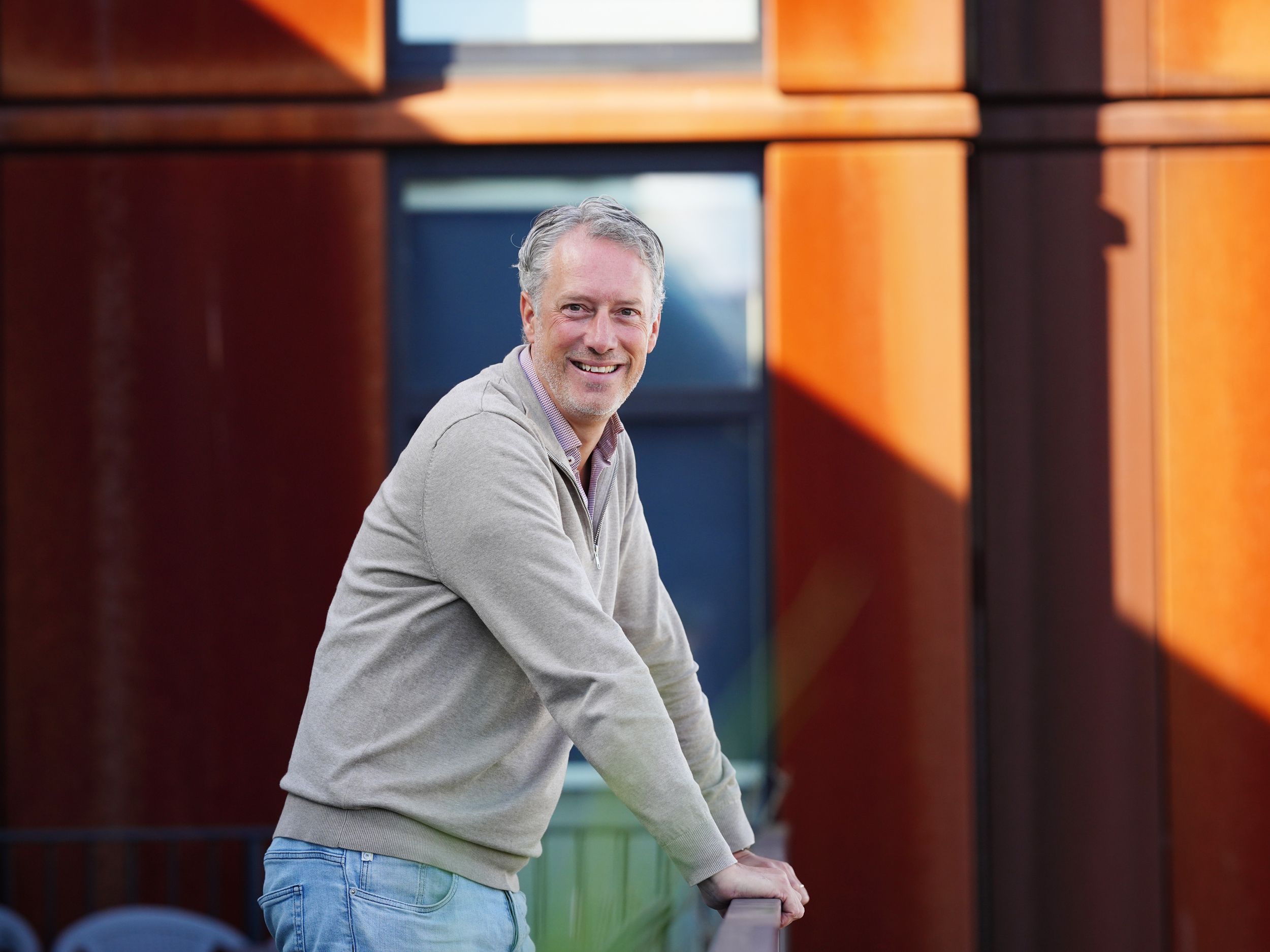 a man is leaning on a railing in front of a building and smiling .