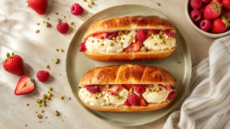 Two brioche buns filled with ice cream, strawberries, raspberries, and pistachios.