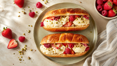 Two brioche buns filled with ice cream, strawberries, raspberries, and pistachios.