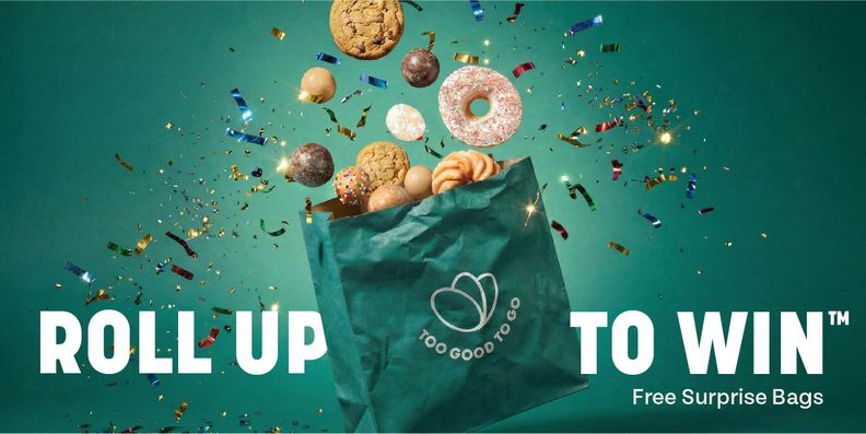 A Too Good To Go bag with baked goods and confetti flying out, above text "ROLL UP TO WIN™ Free Surprise Bags".