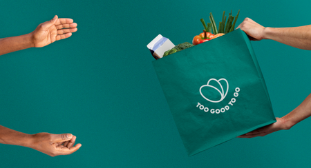 Hands exchanging a Too Good To Go bag full of groceries.