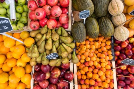 Vibrant market display of fresh fruits: apples, pomegranates, oranges, pears, melons, apricots, and nectarines.