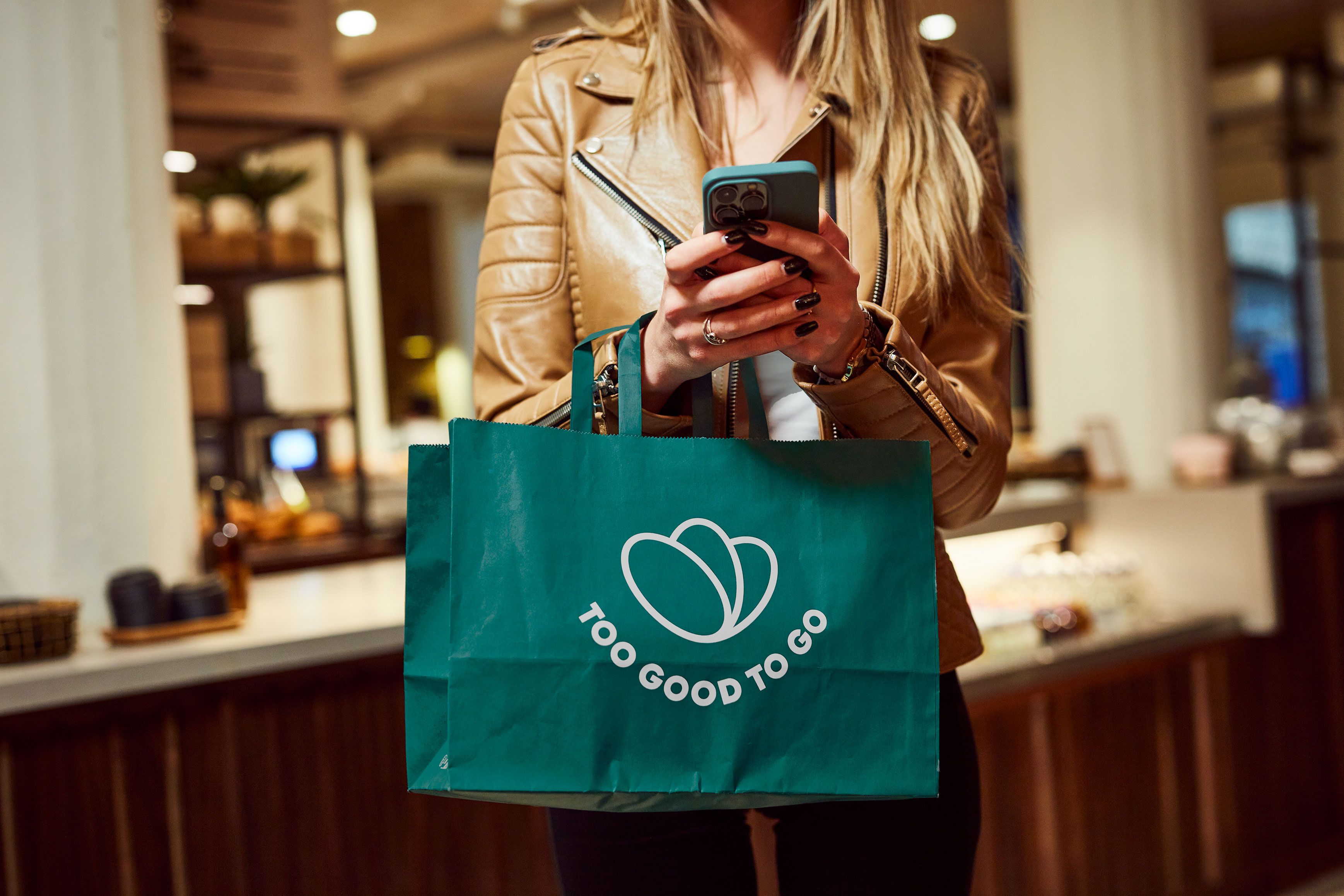 Woman torso holding phone and Too Good To Go branded bag