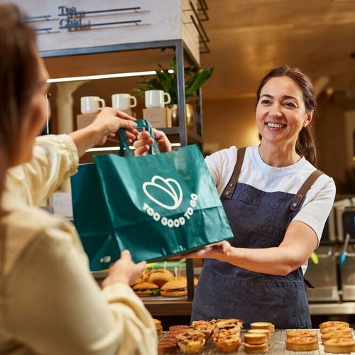 a woman is giving a bag of food to another woman in a bakery .