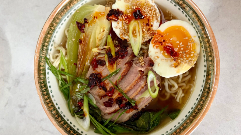 Duck ramen with soft-boiled eggs, bok choy, scallions, and chili oil in a decorative bowl.