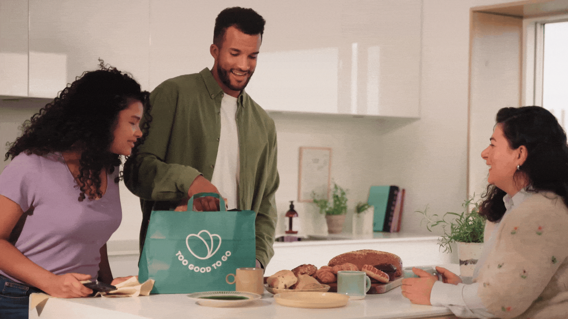 a man is holding a bag of food while two women sit at a table