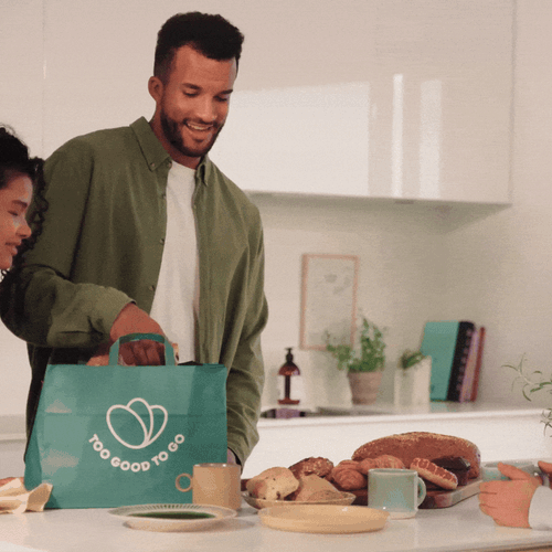 a man is holding a bag of food while two women sit at a table